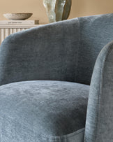 A close up of a stylish, blue velvet upholstered armchair, showcasing its soft texture and curved design.