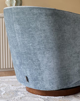 A stylish swivel chair upholstered in a blue fabric, with a wooden base, sits on a patterned rug.