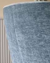 Close-up of a blue fabric armchair, showcasing the textured material and seam detailing. Minimal background with light walls.