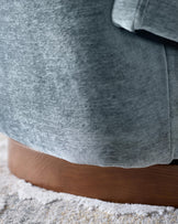 Close-up of a modern swivel chair with grey upholstery and a wooden base, resting on a patterned rug.