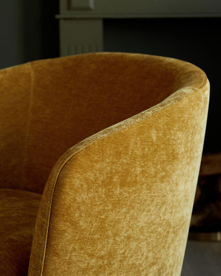 Close-up of a gold velvet armchair, showcasing its texture and curved design. Contemporary and stylish furniture detail.