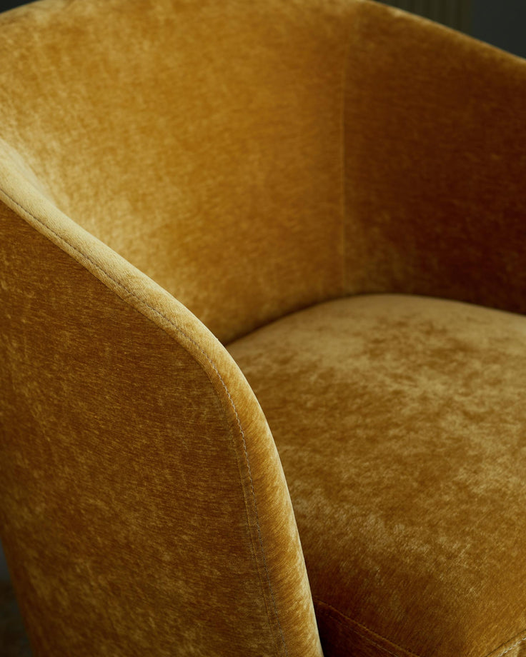 Close up of a golden-yellow velvet armchair, showing the arm and seat cushion.