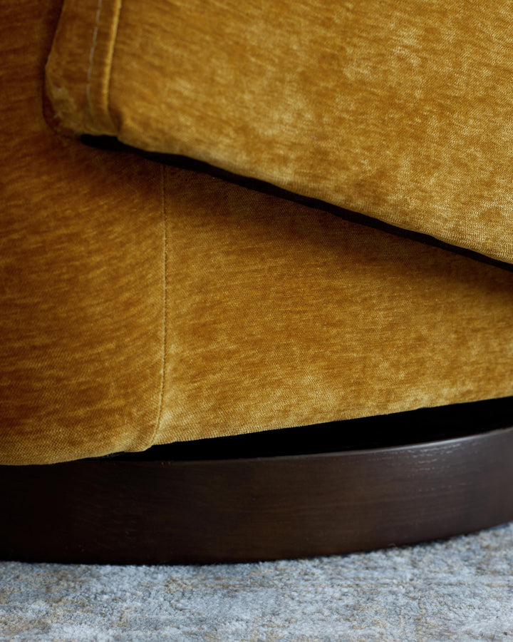 Close-up of a mustard velvet armchair and a dark brown wooden base, resting on a grey textured carpet.