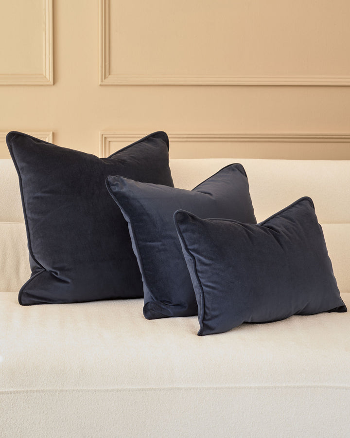 Navy velvet cushion in medium size displayed on a cream sofa against a paneled wall backdrop.