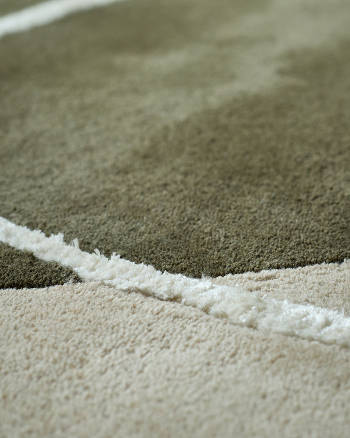 Close up of a cream and green textured rug with a subtle stripe design. Ideal for adding warmth and style to your living space.