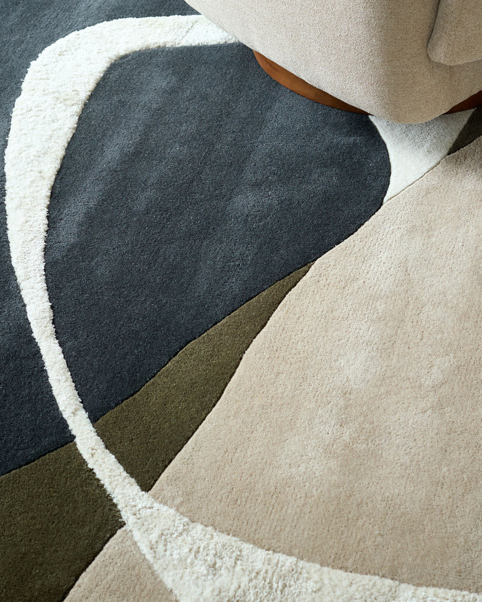 Close-up of a patterned rug with a neutral armchair partially visible in the top right corner.