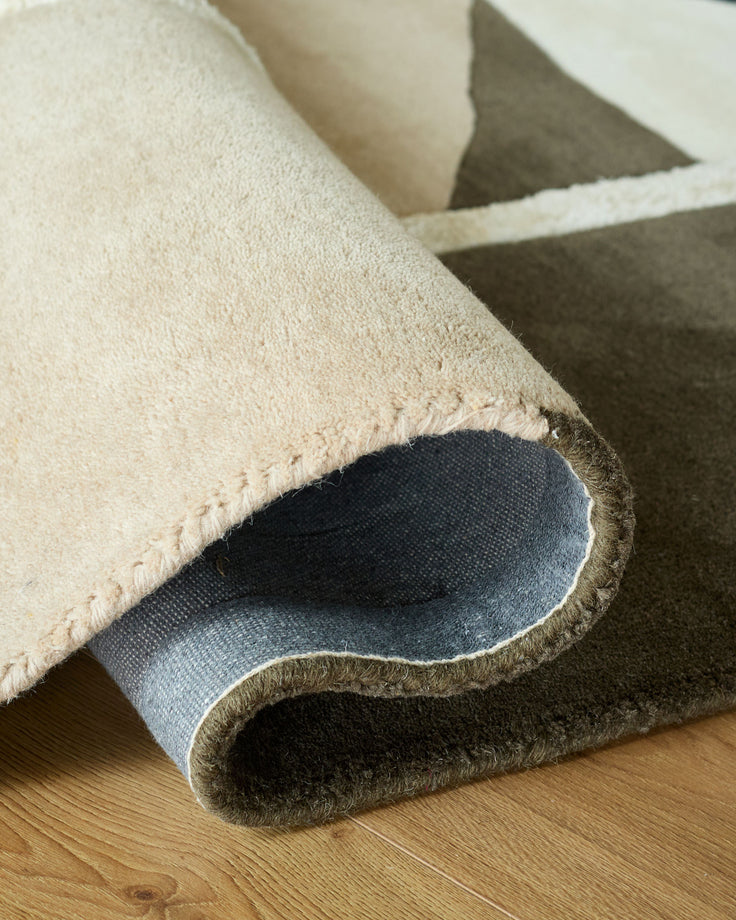A modern rug is partly rolled to display its texture and backing on a wooden floor, showcasing its quality and design.