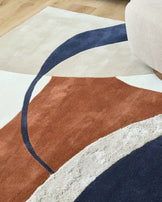 Close-up of a modern rug with cream, brown and navy geometric shapes, plus a beige pouffe.