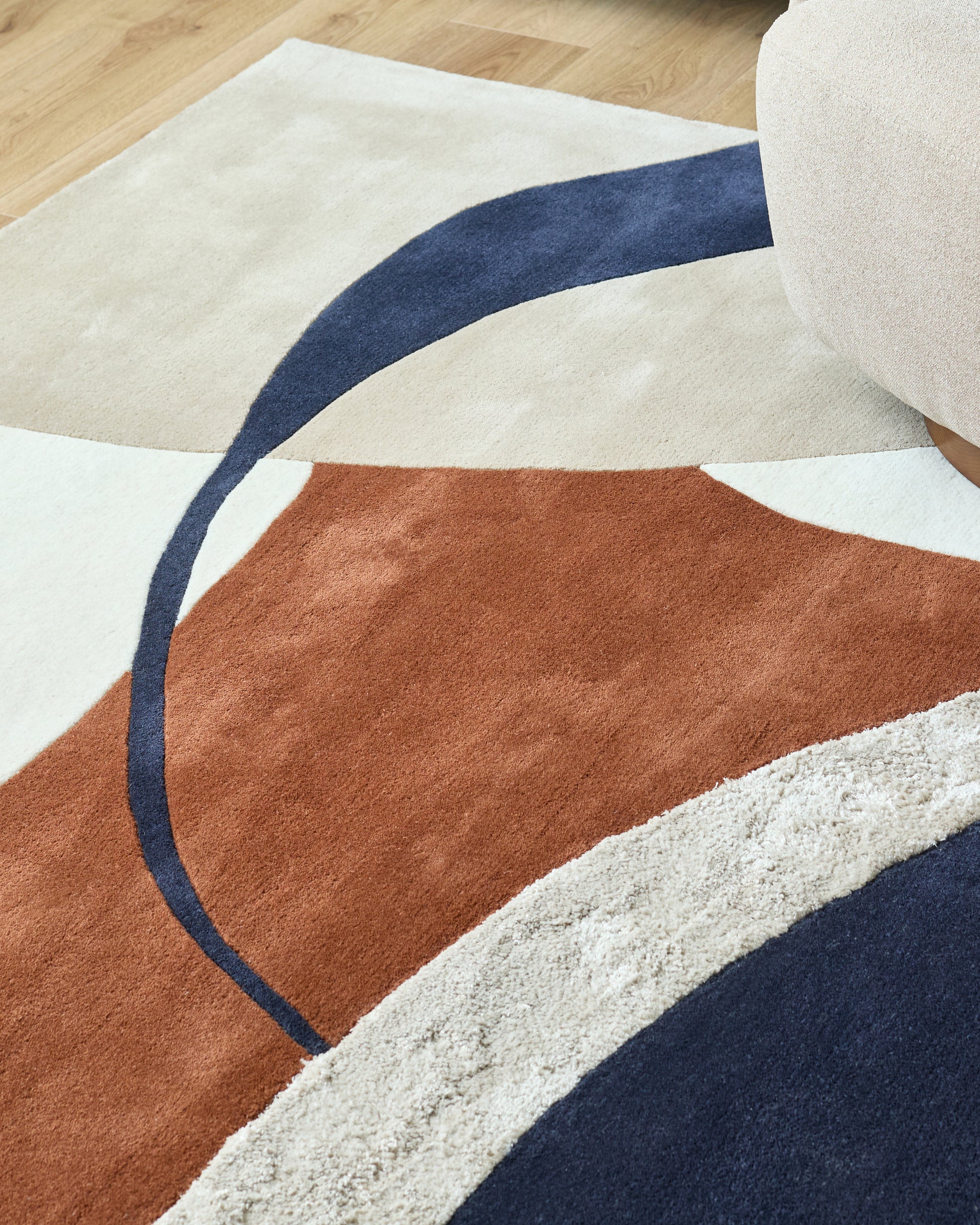 Close-up of a modern rug with cream, brown and navy geometric shapes, plus a beige pouffe.