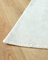 Close-up of a thick, white rug with a textured edge, partially covering a light brown wooden floor.