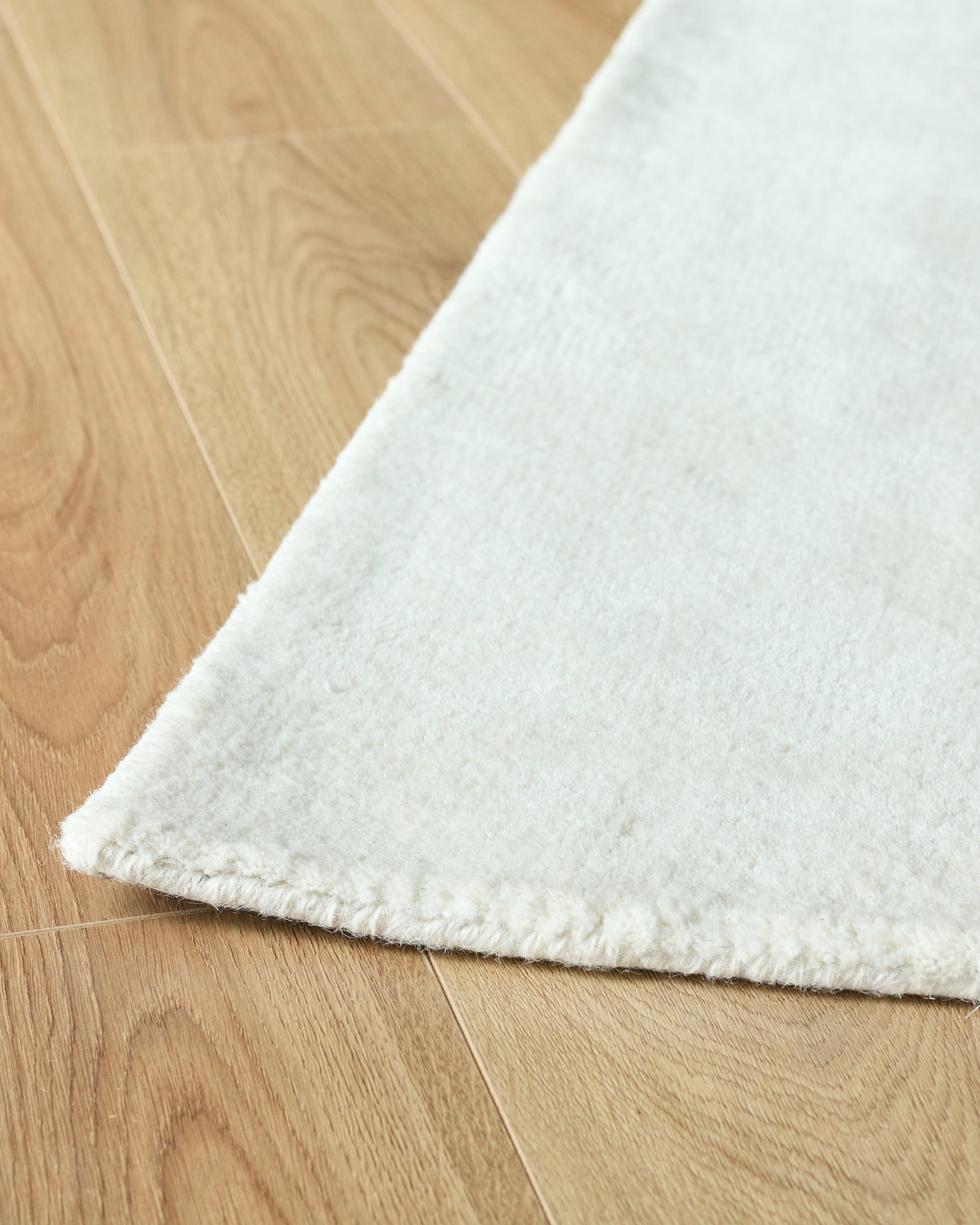 Close-up of a thick, white rug with a textured edge, partially covering a light brown wooden floor.