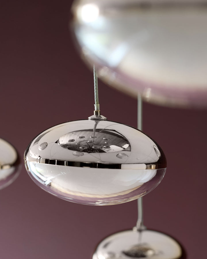 Nina pendant light with clear glass dome shade and chrome metallic hardware, suspended against burgundy background.