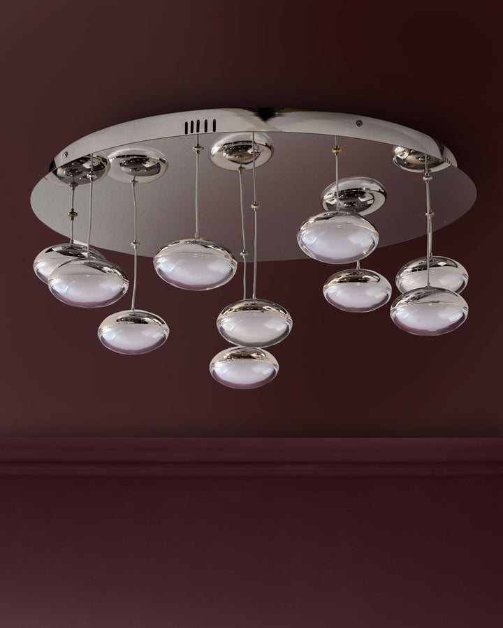 Nina 10-pendant light with chrome finish and frosted glass domes suspended from circular silver canopy against burgundy wall.