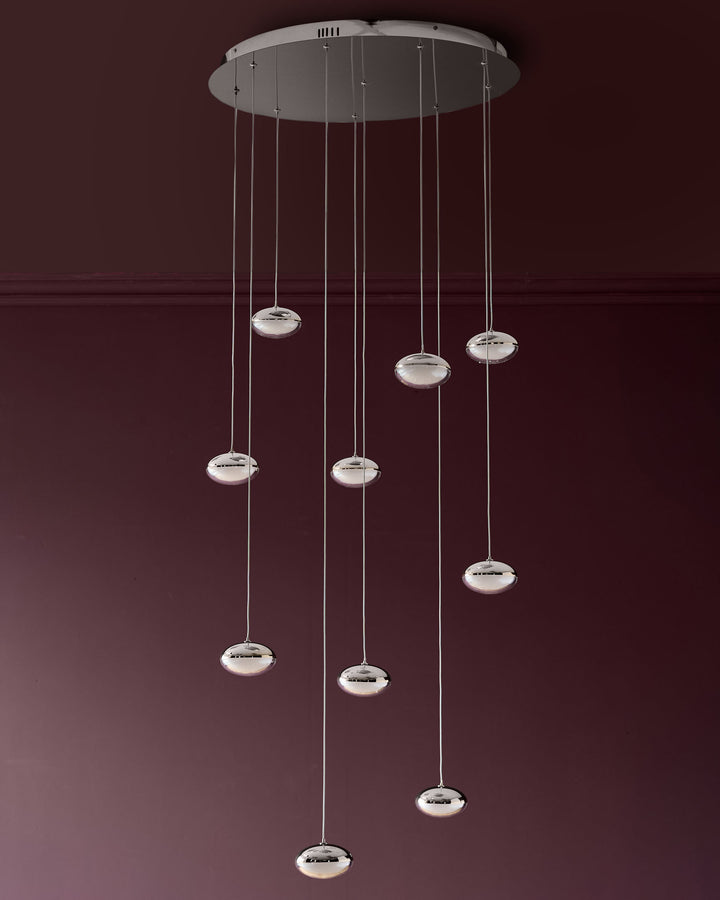 Nina 10-pendant light with chrome finish and frosted glass shades suspended from circular canopy against burgundy wall.