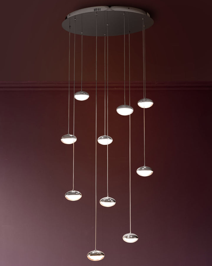Nina 10-pendant light with chrome canopy and ten glass disc shades suspended at varying heights against burgundy wall.