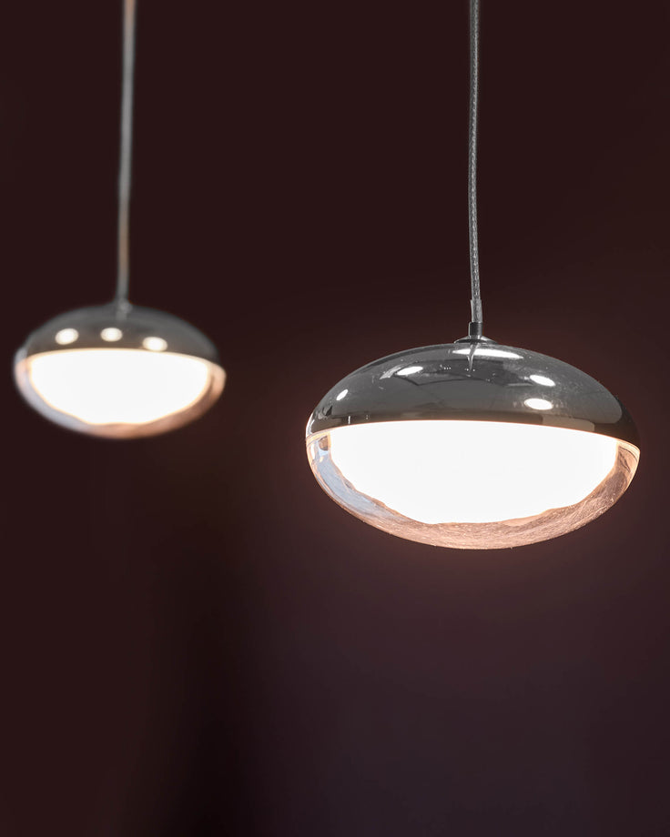 Two modern pendant lights with polished chrome domes and frosted glass diffusers suspended against a dark background.
