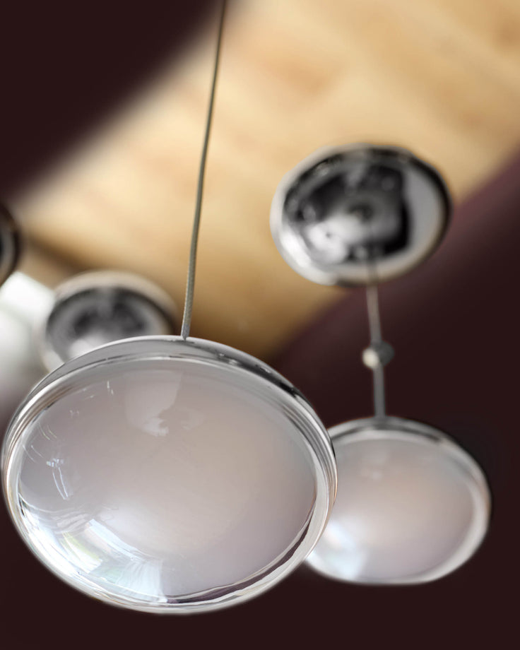 Nina 7 pendant light with clear glass shades and chrome metal fixtures, hanging against warm background.