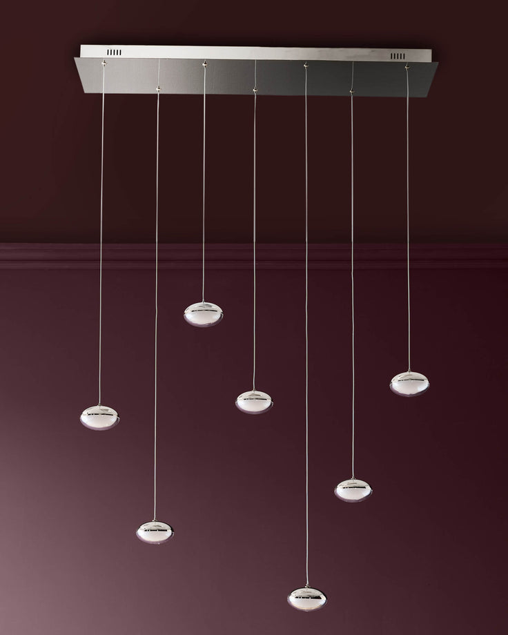 Nina 7-pendant light with chrome finish and frosted glass shades hanging from rectangular canopy against burgundy wall.