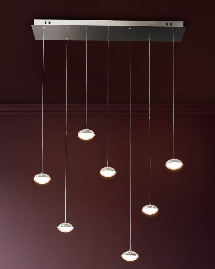 Nina 7-pendant light with chrome finish and glass shades, suspended at varying heights against a burgundy wall.