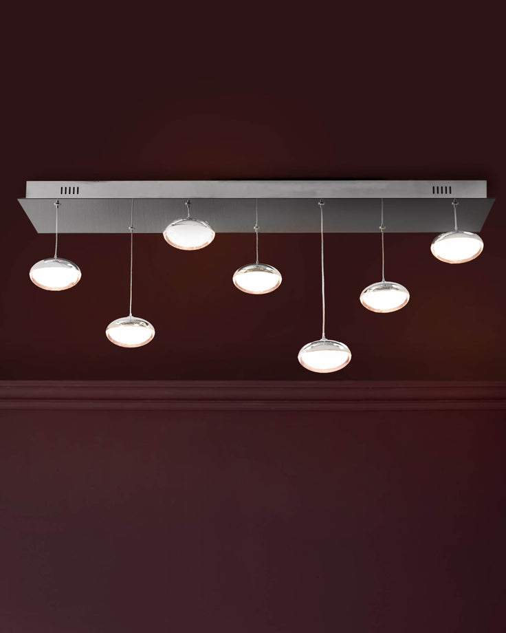 Seven round glass pendant lights with chrome fixtures suspended from a rectangular chrome ceiling plate against a deep burgundy wall.