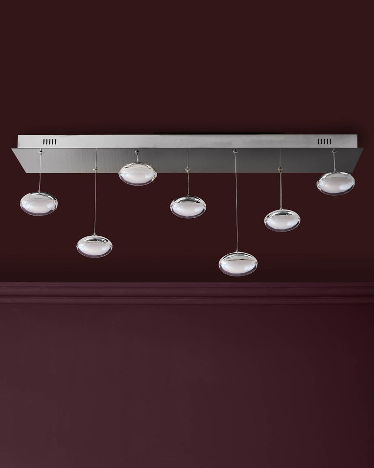 Nina 7-pendant light fixture with clear glass domes and chrome finish against burgundy wall.