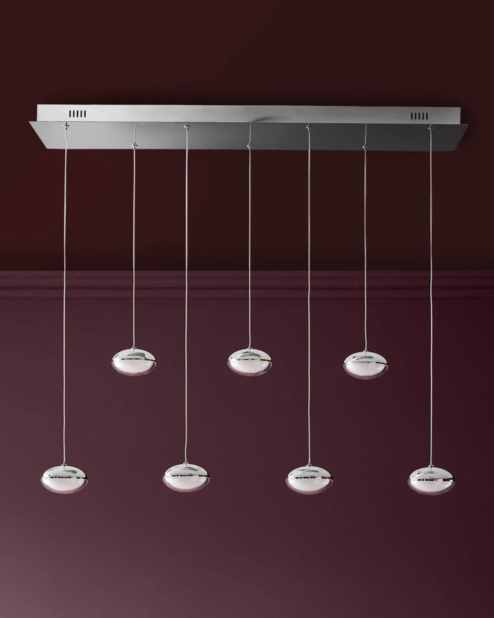 Nina 7-pendant light with chrome finish and white glass shades suspended from silver cables against a burgundy wall.