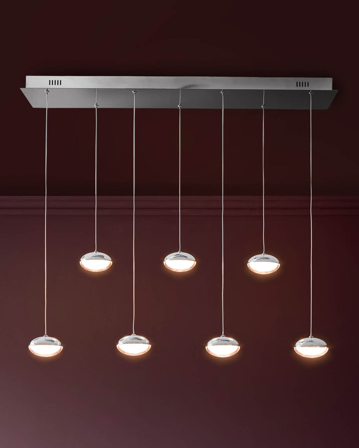 Nina 7-pendant light fixture with chrome finish and glass shades, suspended from adjustable cables against burgundy wall.