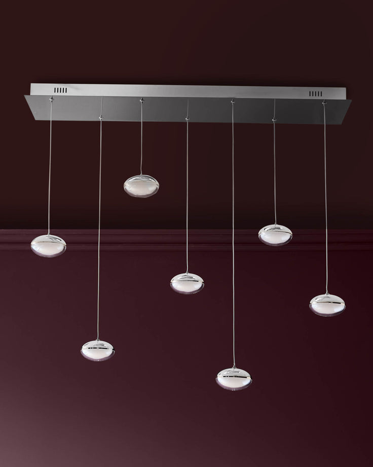 Nina 7-pendant light with round glass shades and chrome finish, suspended from rectangular canopy against burgundy wall.