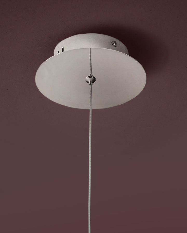 Nina single pendant light with frosted glass diffuser and polished chrome suspension cord against mauve wall.