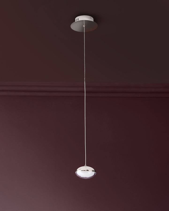 Nina single pendant light with chrome finish and frosted glass shade, suspended by thin wire from ceiling canopy against burgundy wall.