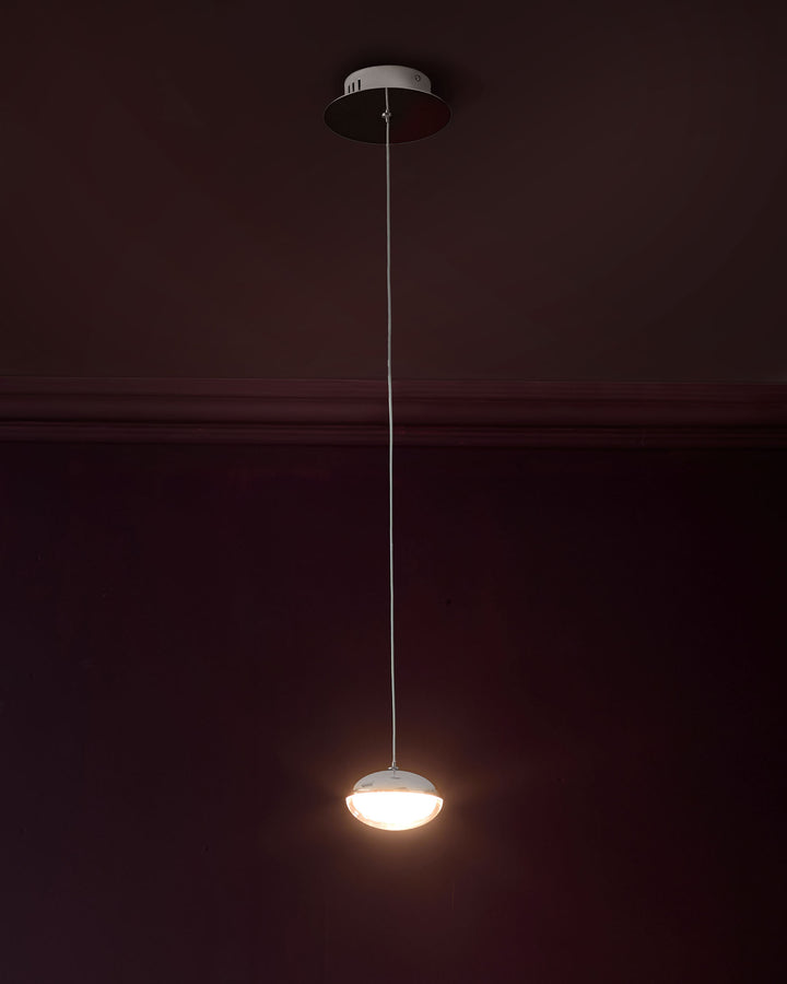 Nina single pendant light with frosted glass dome shade and polished chrome finish, suspended by thin wire against dark wall.