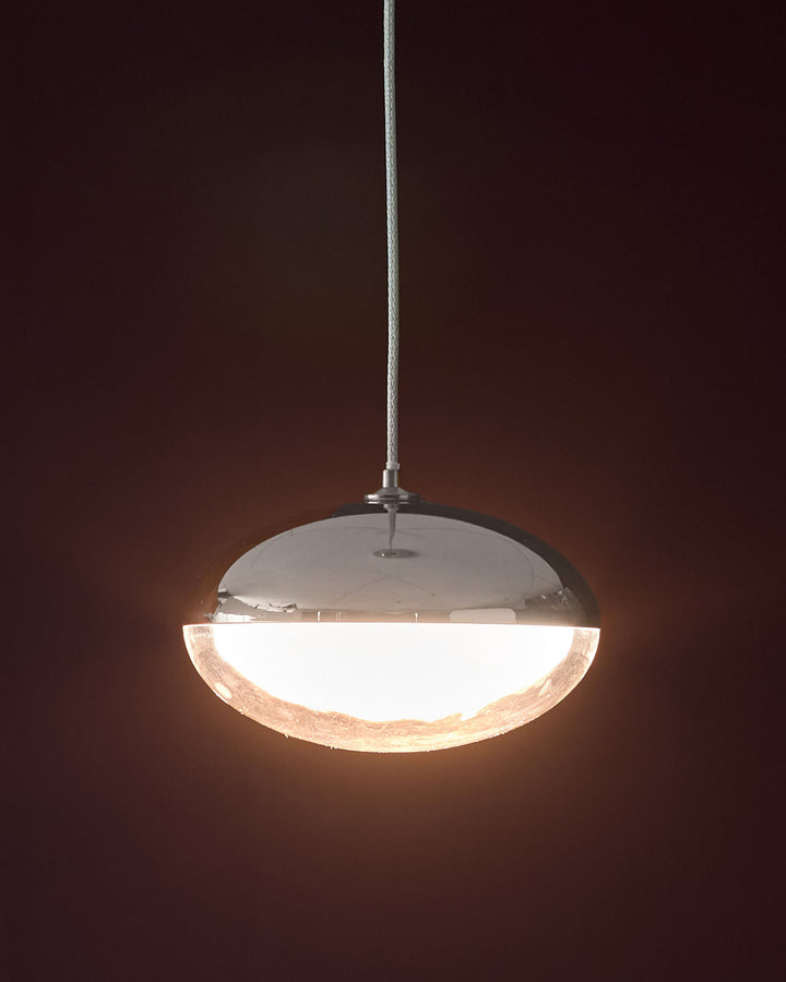 Nina single pendant light in silver chrome with dome-shaped glass shade emitting warm light against dark background.