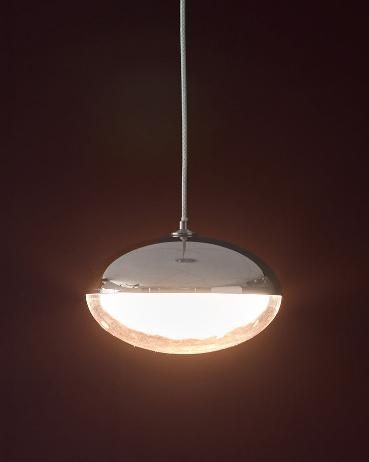 Nina single pendant light in silver chrome with dome-shaped glass shade emitting warm light against dark background.