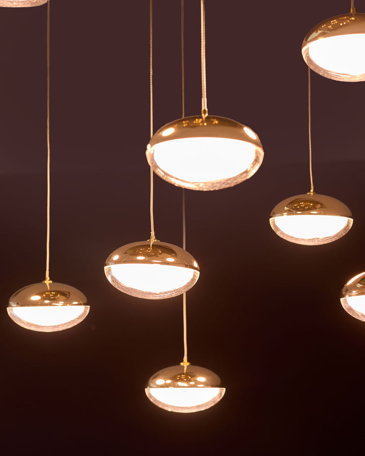 Nina 10 pendant light in soft gold finish with glass diffusers, suspended at varying heights against dark background.