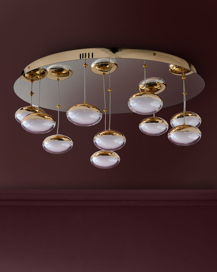 Nina 10-pendant light with soft gold finish and frosted glass domes, suspended from round ceiling canopy against burgundy wall.