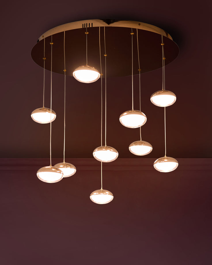 Nina 10-pendant light in soft gold finish with multiple hanging glass disc shades suspended from circular canopy against dark wall.