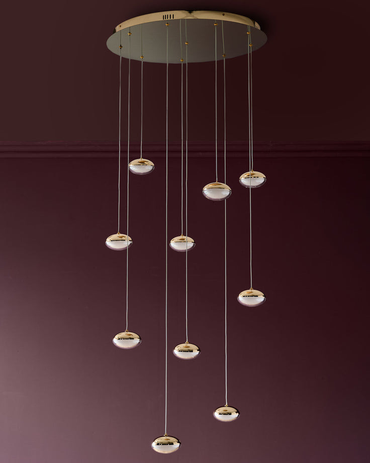 Nina 10-pendant light with soft gold finish and frosted glass shades suspended from ceiling canopy against burgundy wall.