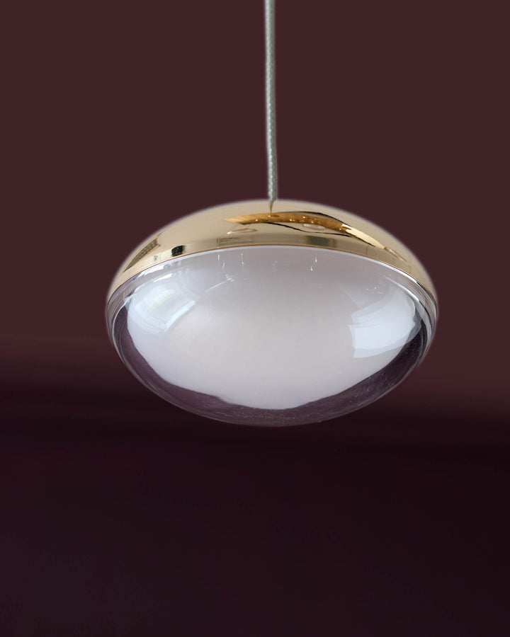 Nina 7 pendant light with frosted glass dome and soft gold metal finish, suspended against burgundy background.