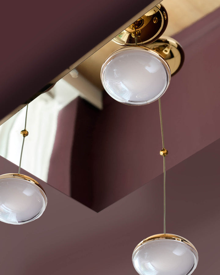 Soft gold ceiling fixture with three clear glass pendant shades hanging at varying lengths against a mauve wall.
