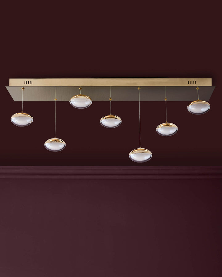 Nina 7-pendant light with soft gold finish and clear glass domes suspended from ceiling fixture against burgundy wall.
