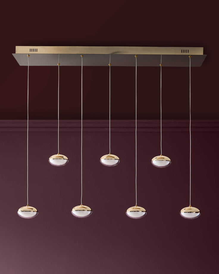 Nina 7-pendant light with soft gold finish and frosted glass shades suspended from a rectangular canopy against burgundy wall.