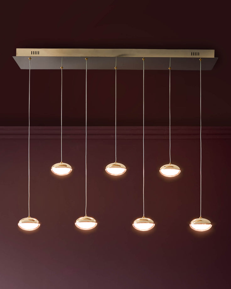 Nina 7-pendant light with soft gold glass shades hanging from a rectangular ceiling canopy against a burgundy wall.