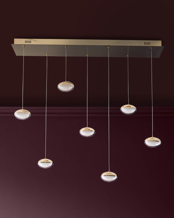 Nina 7-pendant light with soft gold finish and frosted glass shades hanging from rectangular ceiling canopy against burgundy wall.