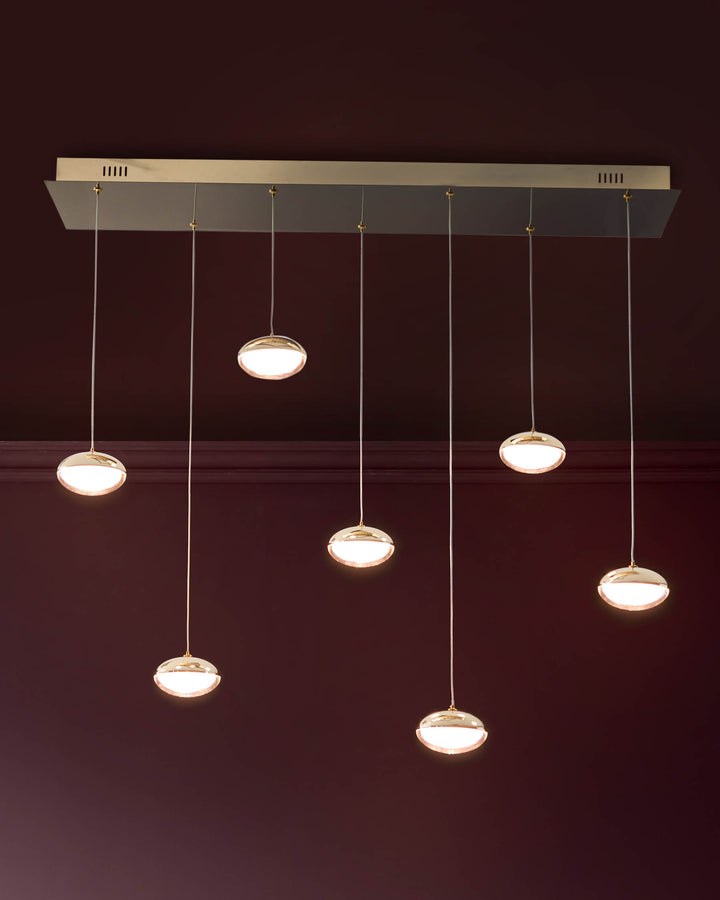 Nina 7-pendant light with soft gold finish and glass shades, suspended from rectangular canopy against burgundy wall.