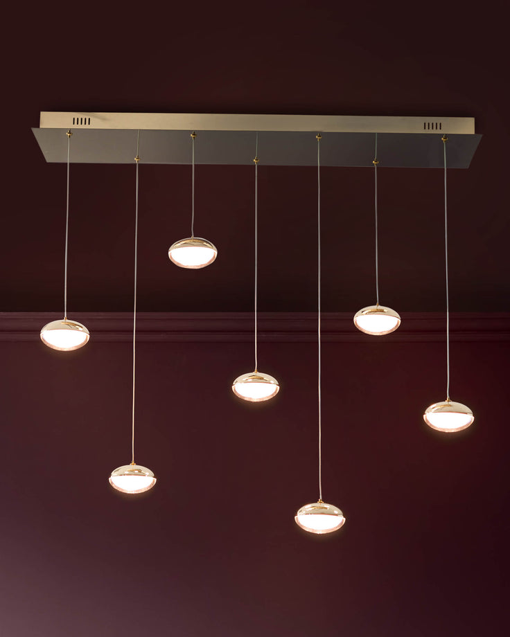 Nina 7-pendant light with soft gold finish and glass shades, suspended from rectangular canopy against burgundy wall.