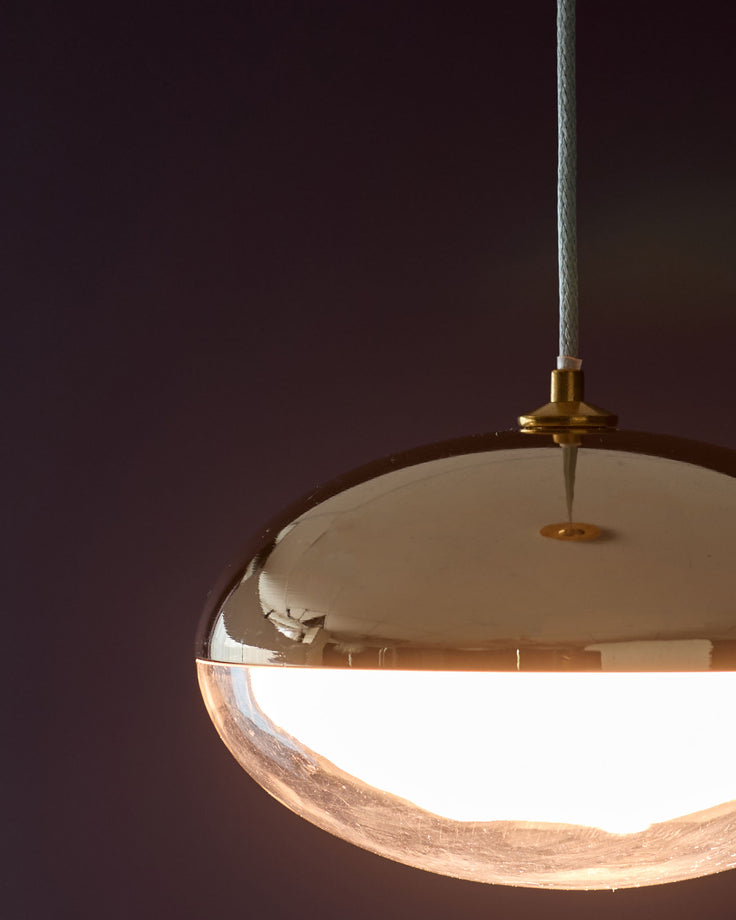 Brass pendant light with cream dome shade and textured wood detail, suspended against burgundy background.