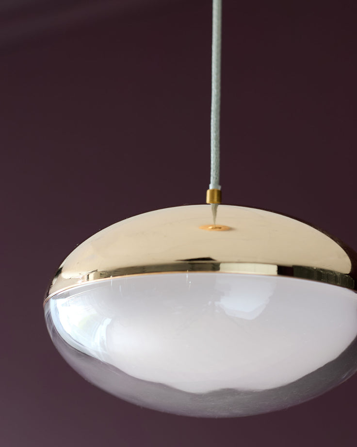 Nina single pendant light with soft gold metal crown and frosted white glass dome, suspended by Grey cord against purple background.