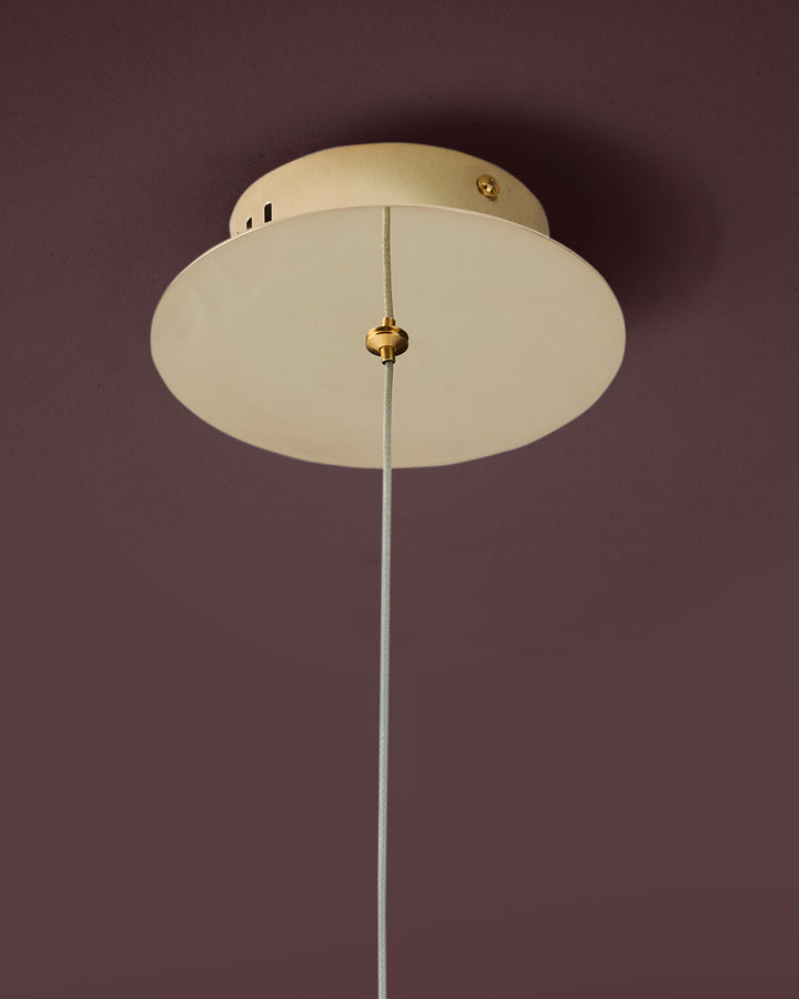 Nina single pendant light in soft gold with frosted glass dome shade and Grey cord against mauve wall.