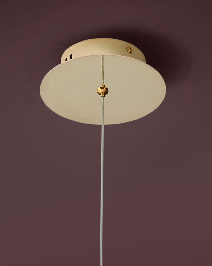 Nina single pendant light in soft gold with frosted glass dome shade and Grey cord against mauve wall.