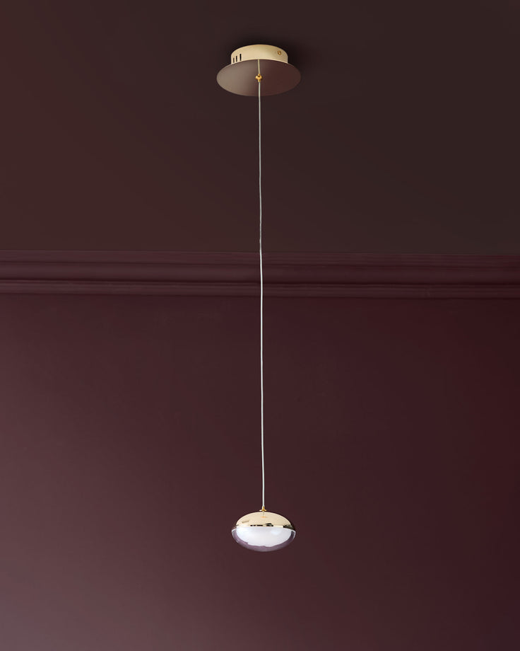 Nina single pendant light in soft gold finish with frosted glass bowl shade, suspended by thin cord from ceiling canopy.